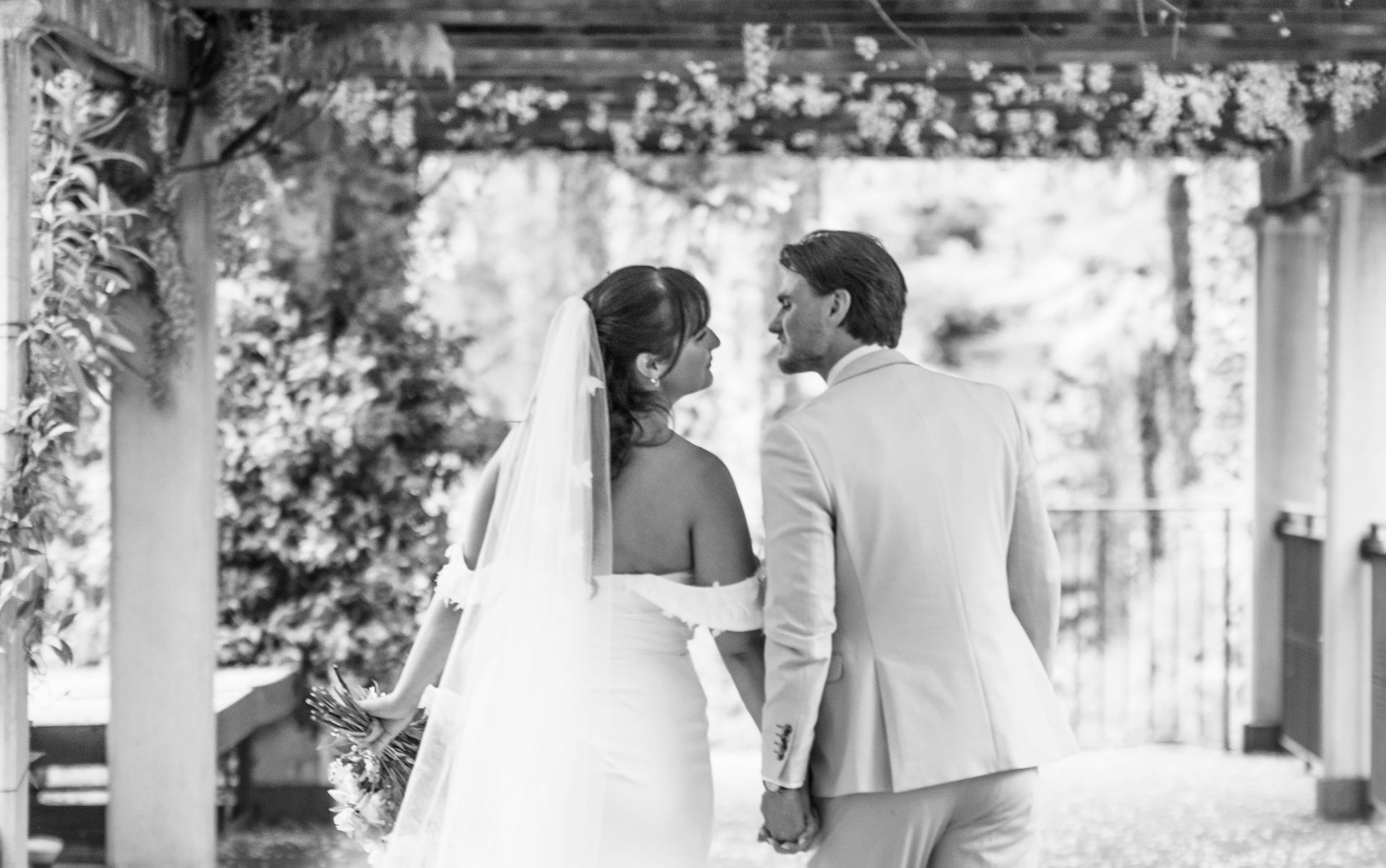 Black and white photograph of a bride and groom under a wisteria pergola